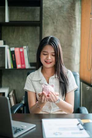 Young woman in office holding a piggy bank, symbolizing savings and financial planning.の写真素材