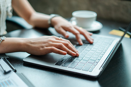 Hands typing on a laptop in a modern office environment with a coffee cup nearby, symbolizing productivity and technology.の写真素材