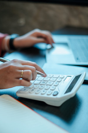 Person calculating finances with a calculator and laptop, focusing on budgeting and financial analysis.の写真素材