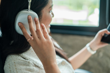 A woman listens to music with headphones in a car, enjoying a relaxing journey on a bright, sunny...