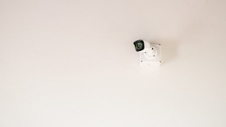 A sleek security camera mounted on a white ceiling, showcasing modern surveillance technology in a...
