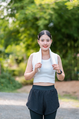 A young woman in sportswear jogging in a green park, showcasing fitness and a healthy lifestyle.の写真素材