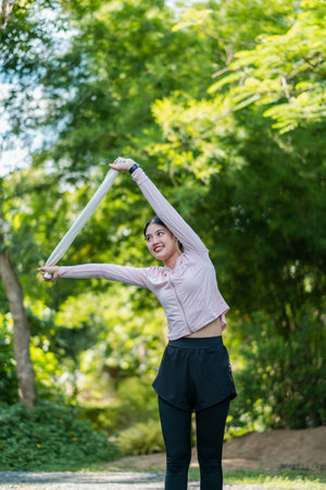 Woman in athletic wear stretching in a park, surrounded by lush greenery, enjoying a sunny day.の写真素材