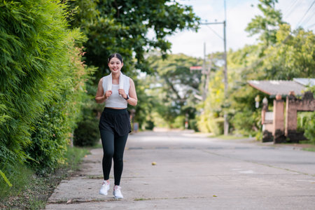 Woman jogging on a quiet suburban street, surrounded by greenery, promoting fitness and healthy lifestyle.の写真素材