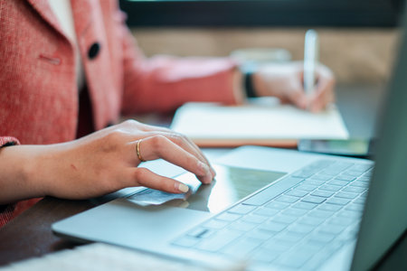 Close-up of a professional working on a laptop and writing notes, showcasing productivity and modern office work.の写真素材