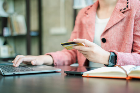 A person in a pink blazer using a laptop and holding a credit card, representing online shopping and business transactions.の写真素材