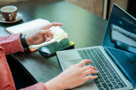 Individual using a laptop and credit card for online shopping in a cozy cafe environment.の写真素材