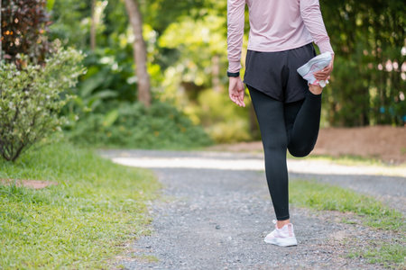 A woman in athletic wear stretches her leg on a gravel path surrounded by greenery, preparing for a workout.の写真素材