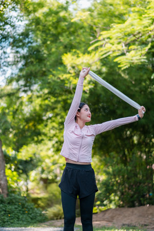 A woman in sportswear stretches in a park surrounded by vibrant greenery, enjoying a sunny day outdoors.の写真素材