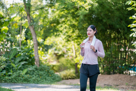 Woman in activewear with towel, enjoying a refreshing walk in a green park setting.の写真素材