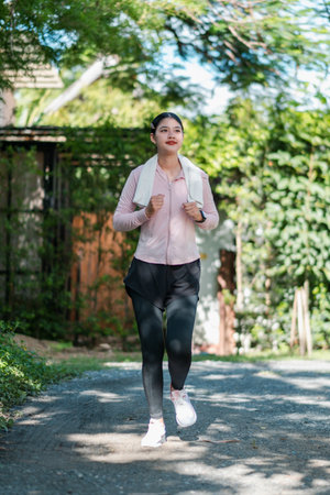 A young woman jogging on a path surrounded by lush greenery, enjoying a sunny day outdoors.の写真素材
