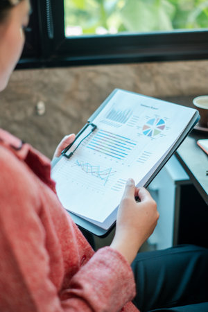 A business professional reviews financial charts and graphs on a clipboard, highlighting data analysis in a modern office environment.の写真素材