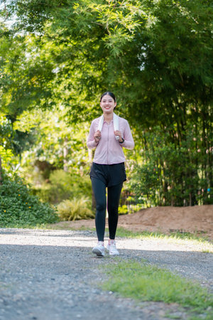 A woman in athletic wear walking on a path surrounded by greenery, enjoying a peaceful morning in the park.の写真素材
