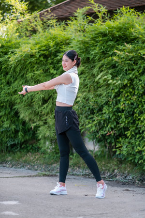 Woman in sporty attire stretching outside, surrounded by lush greenery, promoting fitness and healthy lifestyle.の写真素材