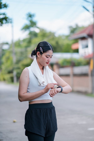 A young woman in athletic wear checks her fitness tracker while exercising outdoors in a suburban area.の写真素材