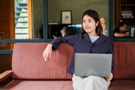 Woman sitting on a sofa with a laptop, enjoying a relaxed work-from-home environment in a modern living room.の写真素材
