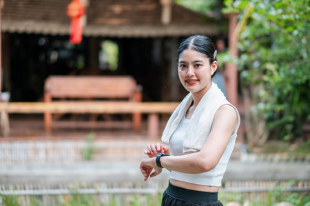 A young woman in sportswear with a fitness tracker, standing outdoors in a natural setting, smiling and relaxed.の写真素材