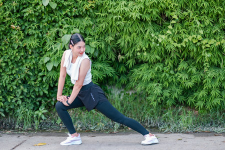 Woman in athletic wear stretching outdoors against a backdrop of vibrant green foliage, promoting fitness and wellness.の写真素材
