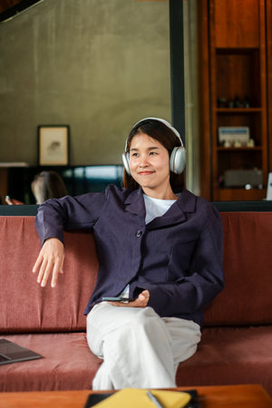 Woman enjoying music with headphones, sitting on a sofa in a stylish living room, exuding relaxation and comfort.の写真素材