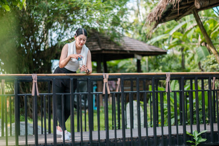 A woman stands on a wooden balcony, sipping a drink, surrounded by tropical plants and greenery.の写真素材