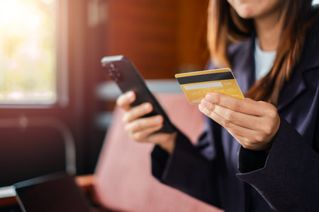 Woman using smartphone and credit card for online shopping in a cafe, highlighting digital payment and e-commerce.の写真素材