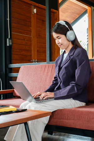 Woman wearing headphones working on a laptop in a modern office setting, showcasing remote work or online learning.の写真素材