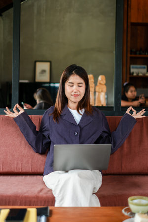 Woman practicing meditation while working on a laptop in a cozy cafe, embodying balance and mindfulness in a modern lifestyle.の写真素材