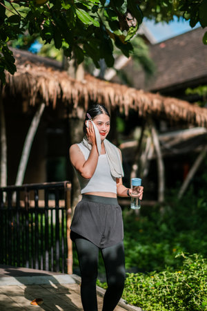 Woman in athletic wear with water bottle, enjoying a sunny day in a green park setting.の写真素材