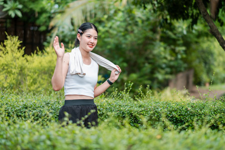 A young woman in athletic attire smiles while exercising in a vibrant, green park, showcasing a healthy and active lifestyle.の写真素材