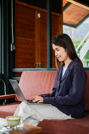 Woman focused on laptop work in a modern home office, surrounded by natural light and cozy decor.の写真素材