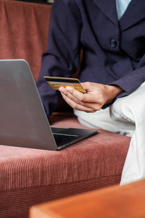 Close-up of a person holding a credit card while using a laptop, depicting online shopping in a cozy home environment.の写真素材