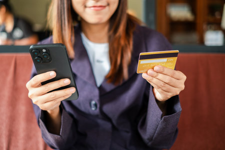 Close-up of a woman using a smartphone and credit card for online shopping in a relaxed cafe environment.の写真素材