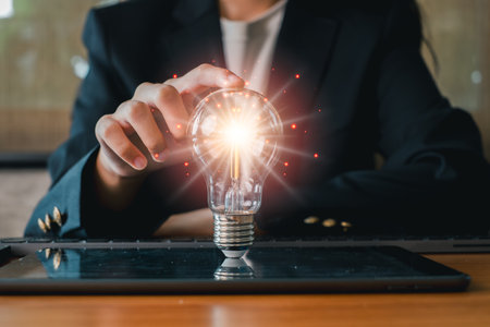 A businessperson in a suit touches a glowing light bulb on a tablet, representing innovation and technology in a modern business setting.の写真素材