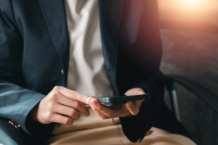 Close-up of a business professional using a smartphone in an office environment with warm sunlight.の写真素材