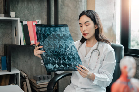 Female doctor examines X-ray in a well-lit medical office, showcasing modern healthcare professionalism.の写真素材
