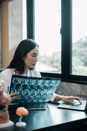 A focused female doctor examines X-ray images at her desk in a bright, modern medical office.