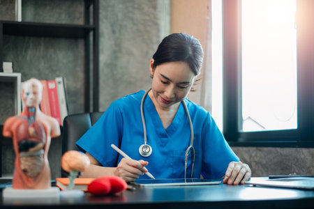 A healthcare worker in blue scrubs uses a tablet in a contemporary medical office setting.