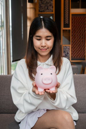 Young woman in casual attire holding a pink piggy bank, symbolizing savings and financial planning.の写真素材