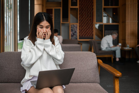 Surprised young woman looking at laptop screen in a cozy cafe setting with wooden decor and relaxed ambiance.の写真素材
