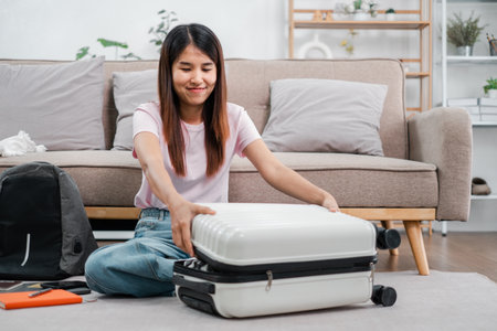 Smiling woman packing suitcase in a stylish living room, preparing for a travel adventure. Modern decor and cozy atmosphere.の写真素材