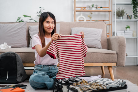 Young woman packing a suitcase in a cozy living room, preparing for a travel adventure. Casual style with a striped shirt.の写真素材