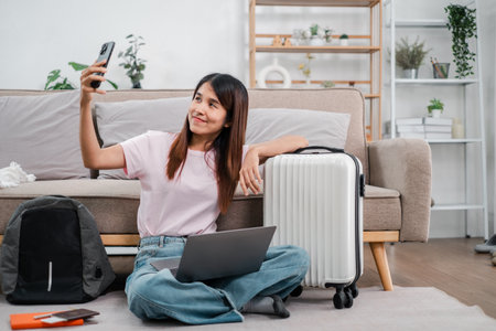 Smiling woman sitting on the floor with suitcase and laptop, capturing a selfie before travel.の写真素材