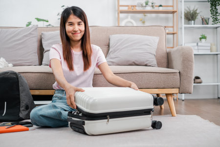 Smiling woman packing a suitcase in a cozy living room, preparing for a travel adventure. Casual and relaxed atmosphere.の写真素材