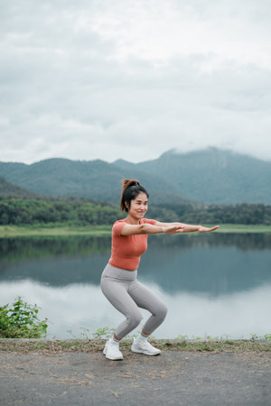 Woman performing squats by a lake with mountains in the background, showcasing outdoor fitness and natural beauty.の写真素材