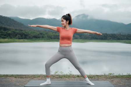 Woman doing yoga by a lake with mountains in the background, showcasing tranquility and fitness in nature.の写真素材