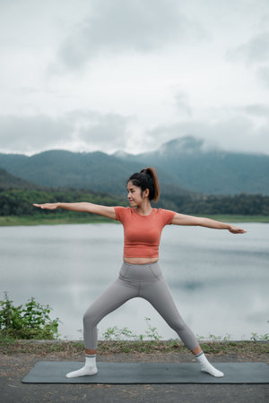 Woman in activewear doing yoga by a lake with mountains in the background, showcasing tranquility...