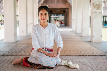 A woman in traditional Thai clothing sits gracefully in a historic temple corridor, showcasing...