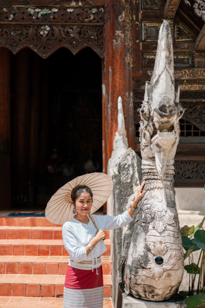 A woman holding a parasol stands beside a detailed stone sculpture at a historic temple, showcasing traditional architecture.の写真素材