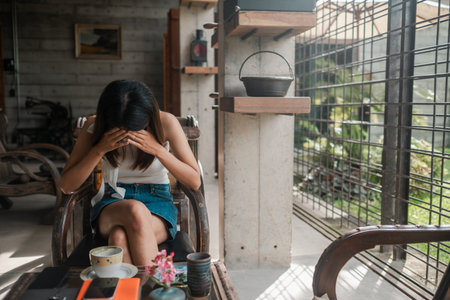 Woman sitting in a modern setting, enjoying a drink and using a smartphone, surrounded by natural light and contemporary decor.の写真素材