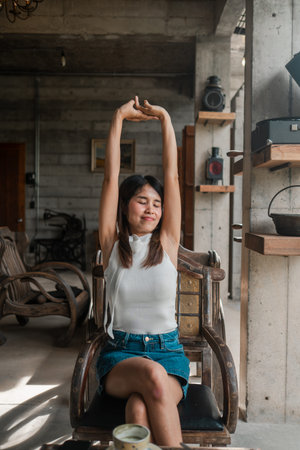 A young woman stretches in a sunlit industrial-style loft, surrounded by vintage decor and rustic...
